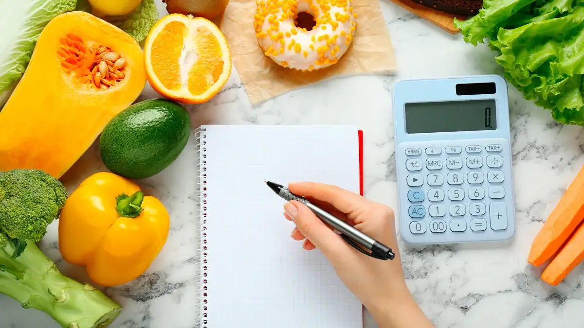 Mujer calculando calorías en mesa de mármol blanco con productos alimenticios, vista superior