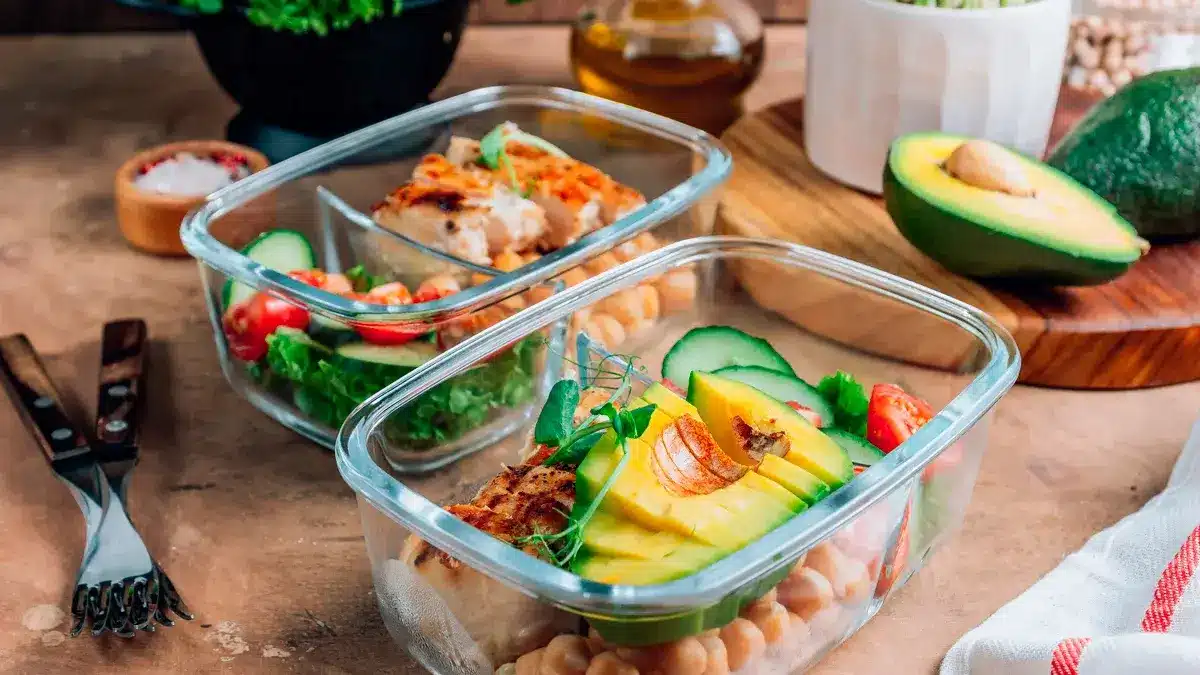 Envasos de preparació per a menjars saludables amb cigrons, pollastre, tomàquets, cogombres i alvocats. Dinar saludable a recipients de vidre sobre fons rústic beix. Concepte d'escombraries zero