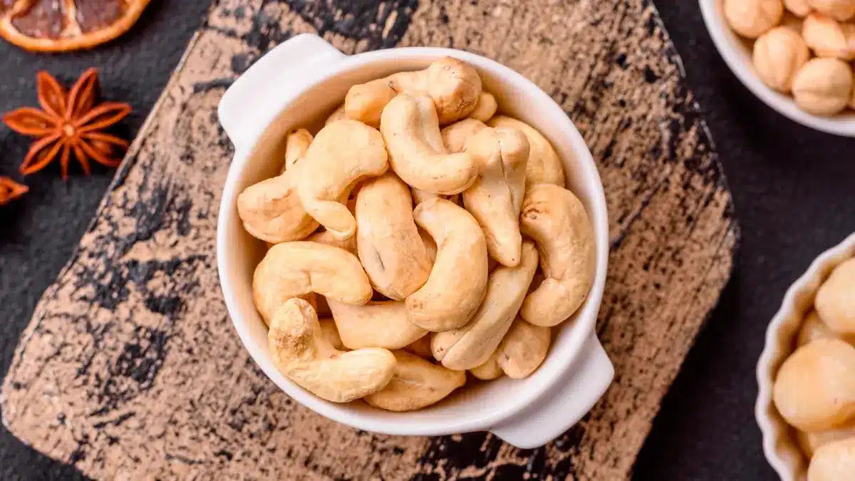 Deliciosas nueces de cajú nutritivas en tazón de cerámica sobre fondo de hormigón oscuro