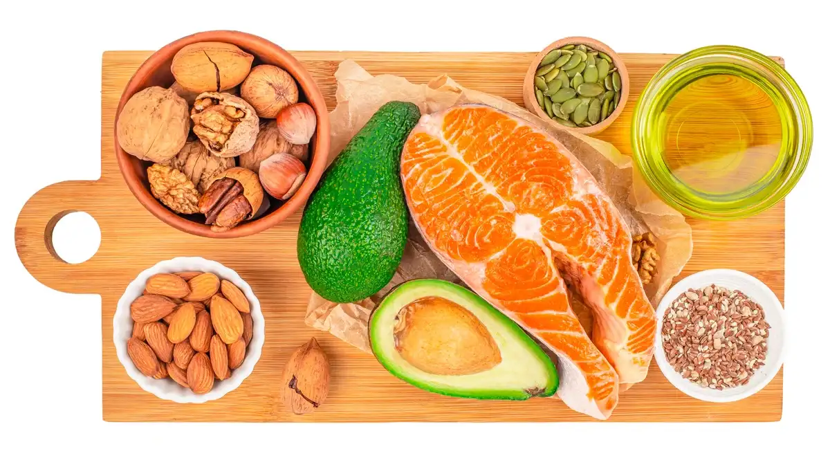 Vista superior de les fonts d'aliments de greixos saludables, inclòs el filet de salmó cru, alvocat, nous, llavors i oli d'oliva disposats en una taula de tallar de fusta, nutrició equilibrada i concepte d'alimentació neta