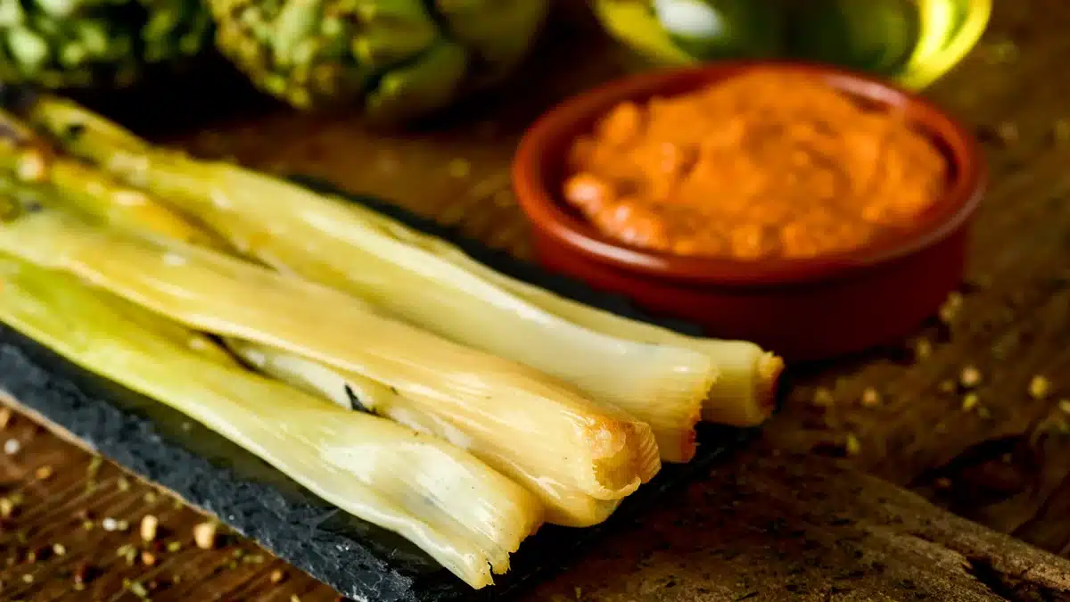 calçots rostits, cebes dolces típiques de Catalunya, Espanya, bol de fang amb salsa romesco per submergir-les, cruixent amb oli d'oliva sobre una taula rústica de fusta