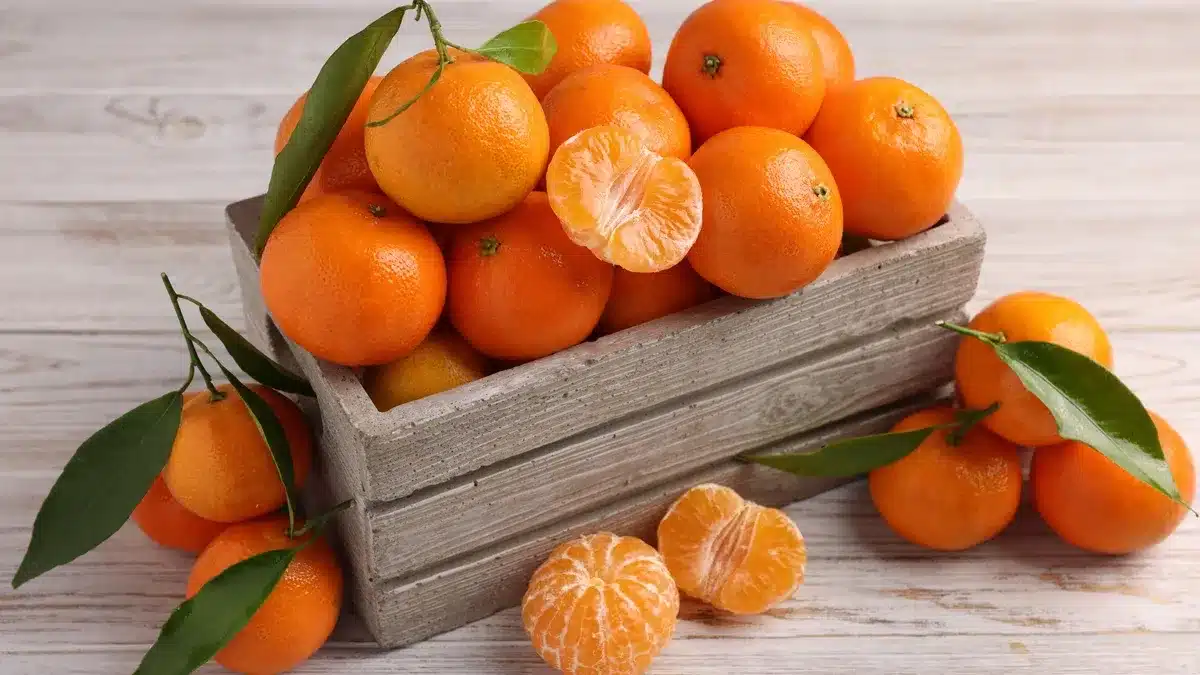 caja de deliciosas mandarinas con hojas sobre mesa de madera clara